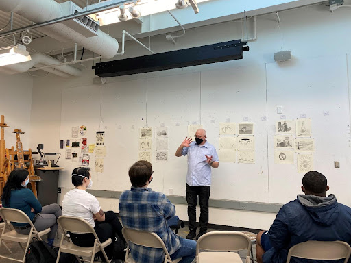 Showcasing student works begins early in the Art Department. Professor Charles Goolsby stands in front of his Introductory Drawing Class during a critique session of their first set of works for the class.